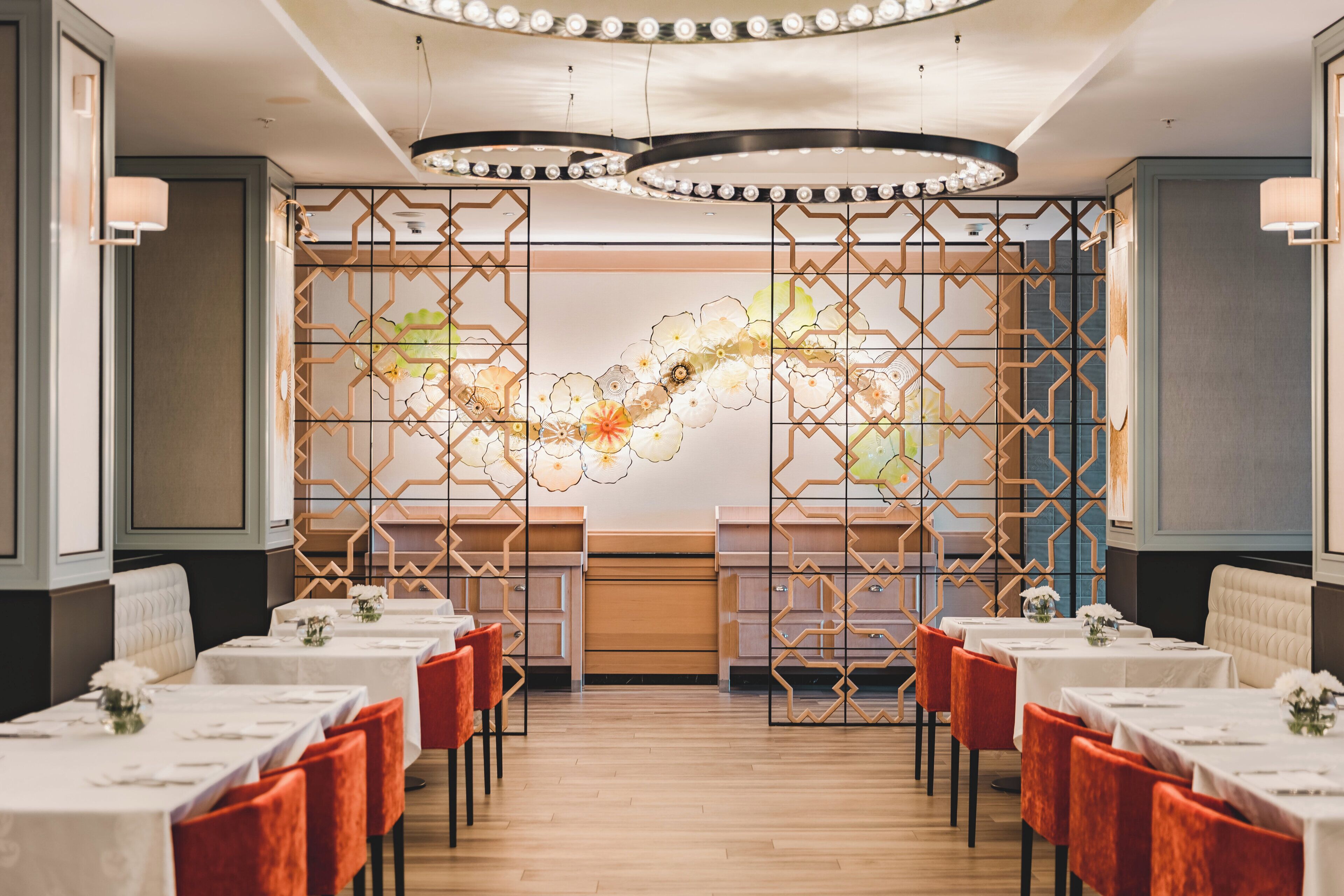 A restaurant with a long table layout, a decorative wall with a floral pattern, and a modern chandelier.