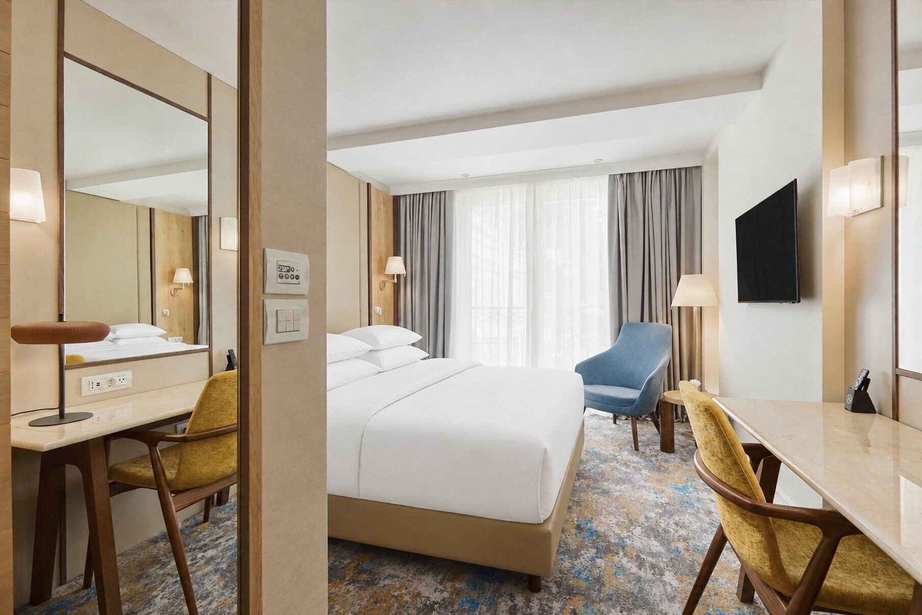 A hotel room with a bed, a desk, a chair, a TV, and a window with curtains.