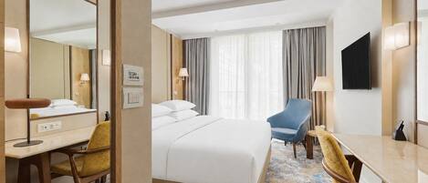 Une chambre d’hôtel avec un lit, un bureau, une chaise, une télévision et une fenêtre avec des rideaux.