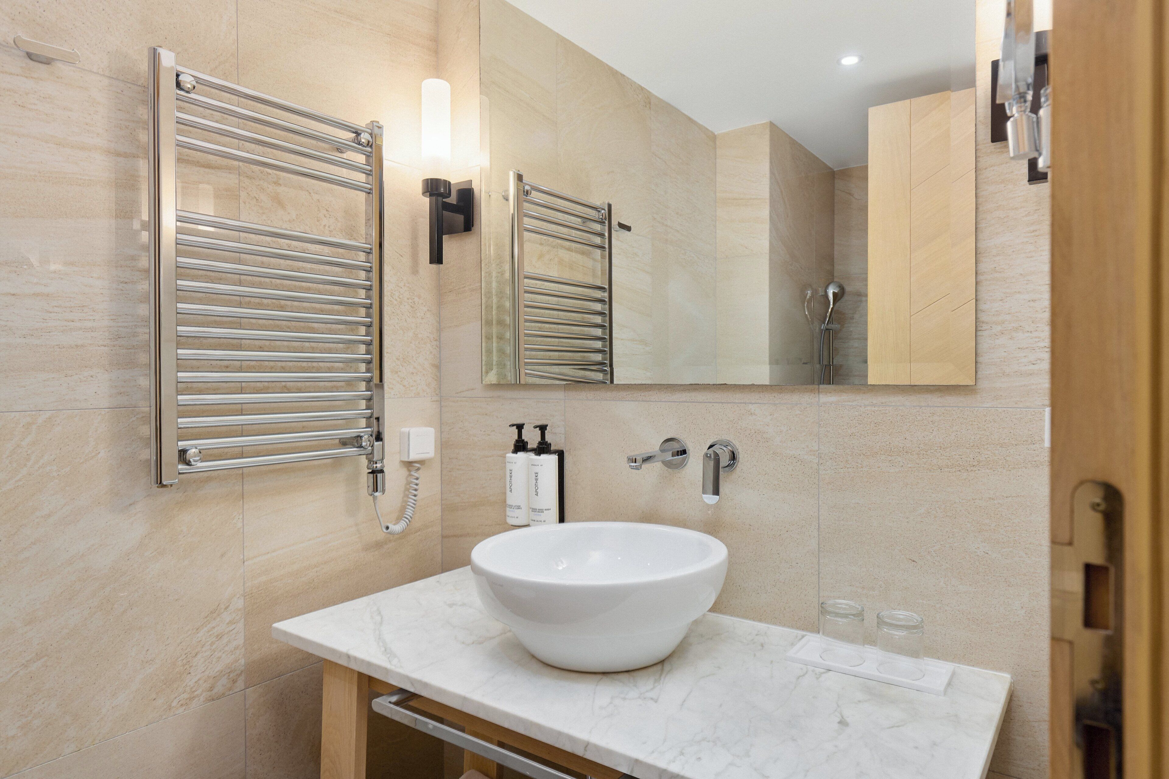 Un baño moderno con un lavabo de mármol blanco, un perchero, un espejo y una zona de ducha.