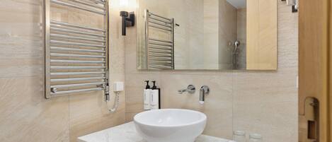Un baño moderno con un lavabo de mármol blanco, un perchero, un espejo y una zona de ducha.