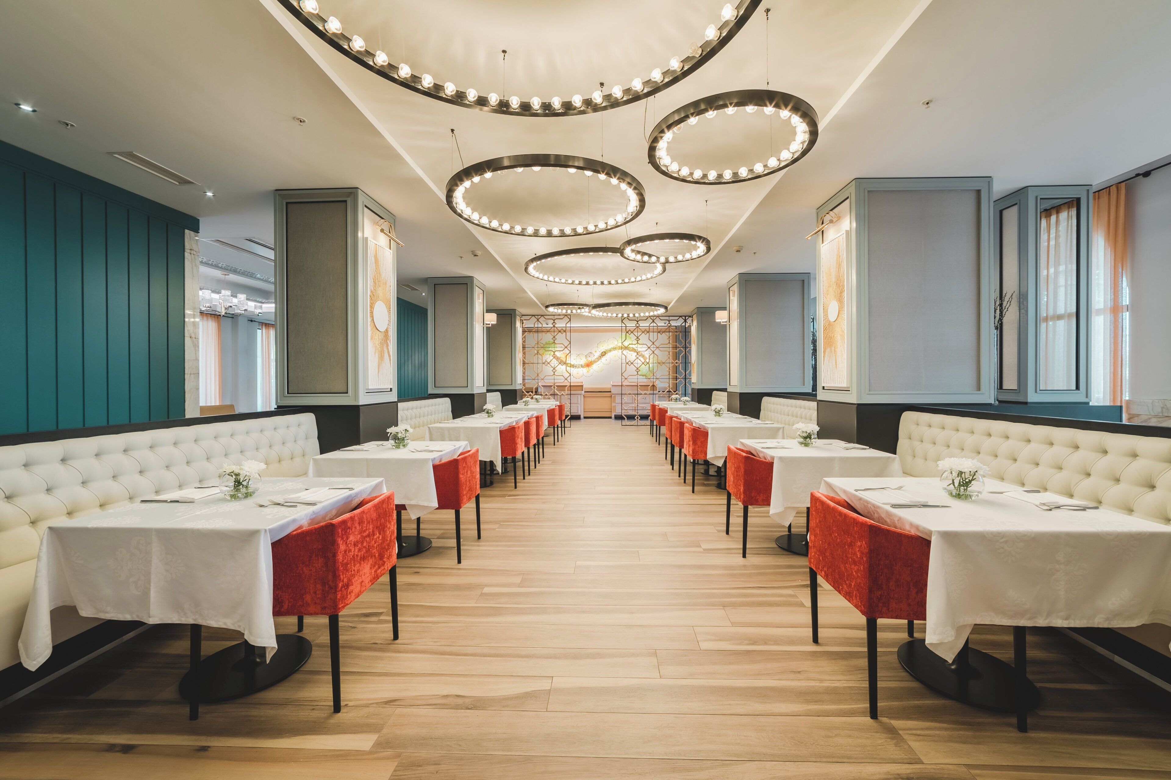 Un restaurant avec une grande table centrale, des nappes blanches, des banquettes rouges recouvertes de tissu et un plancher en bois.