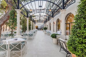 An indoor patio area with tables and chairs, a glass ceiling, and greenery. - Crowne Plaza Budva by IHG (Budva)