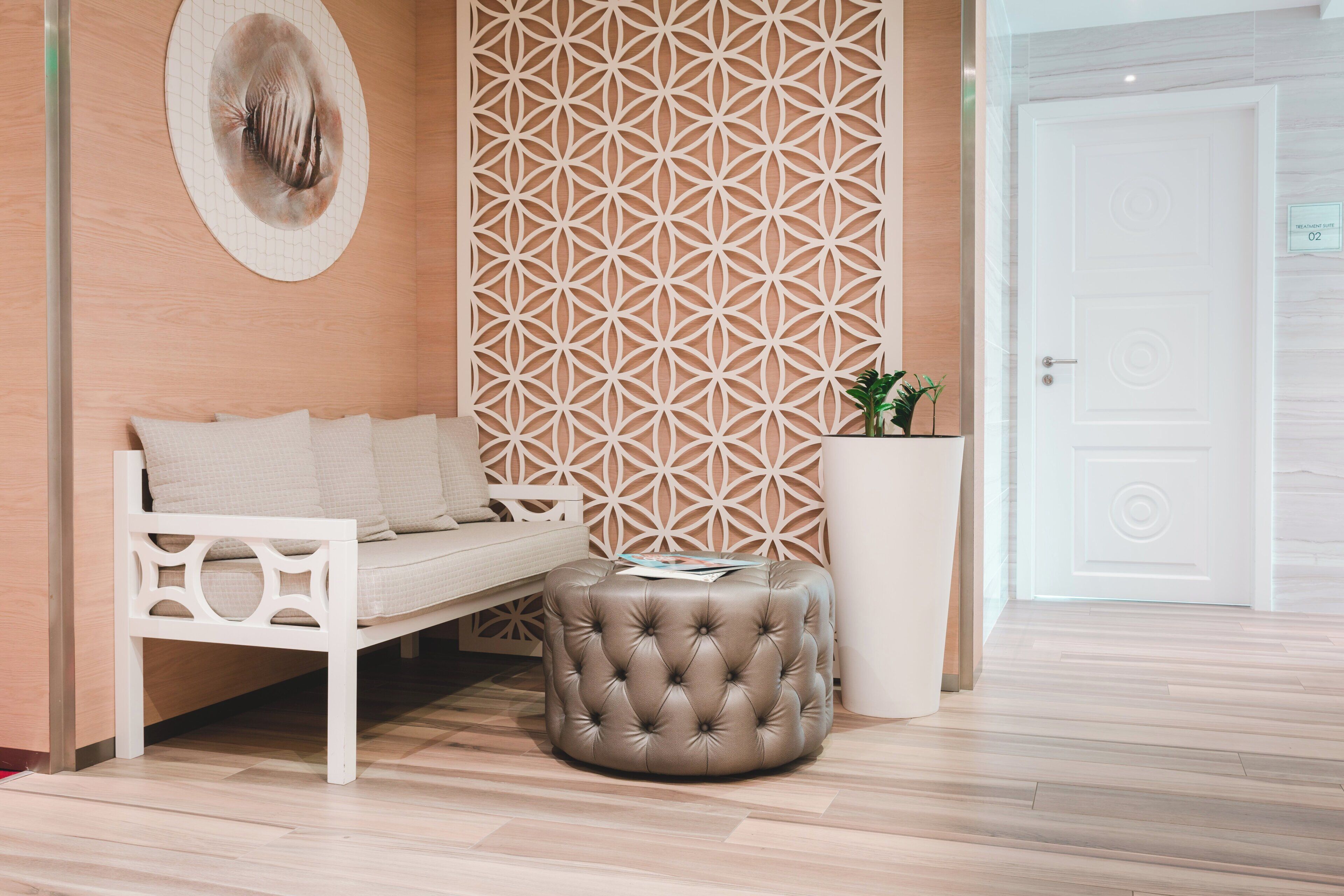 A room with a white sofa, a tufted ottoman, a decorative wall panel, a potted plant, and a door with a number sign.