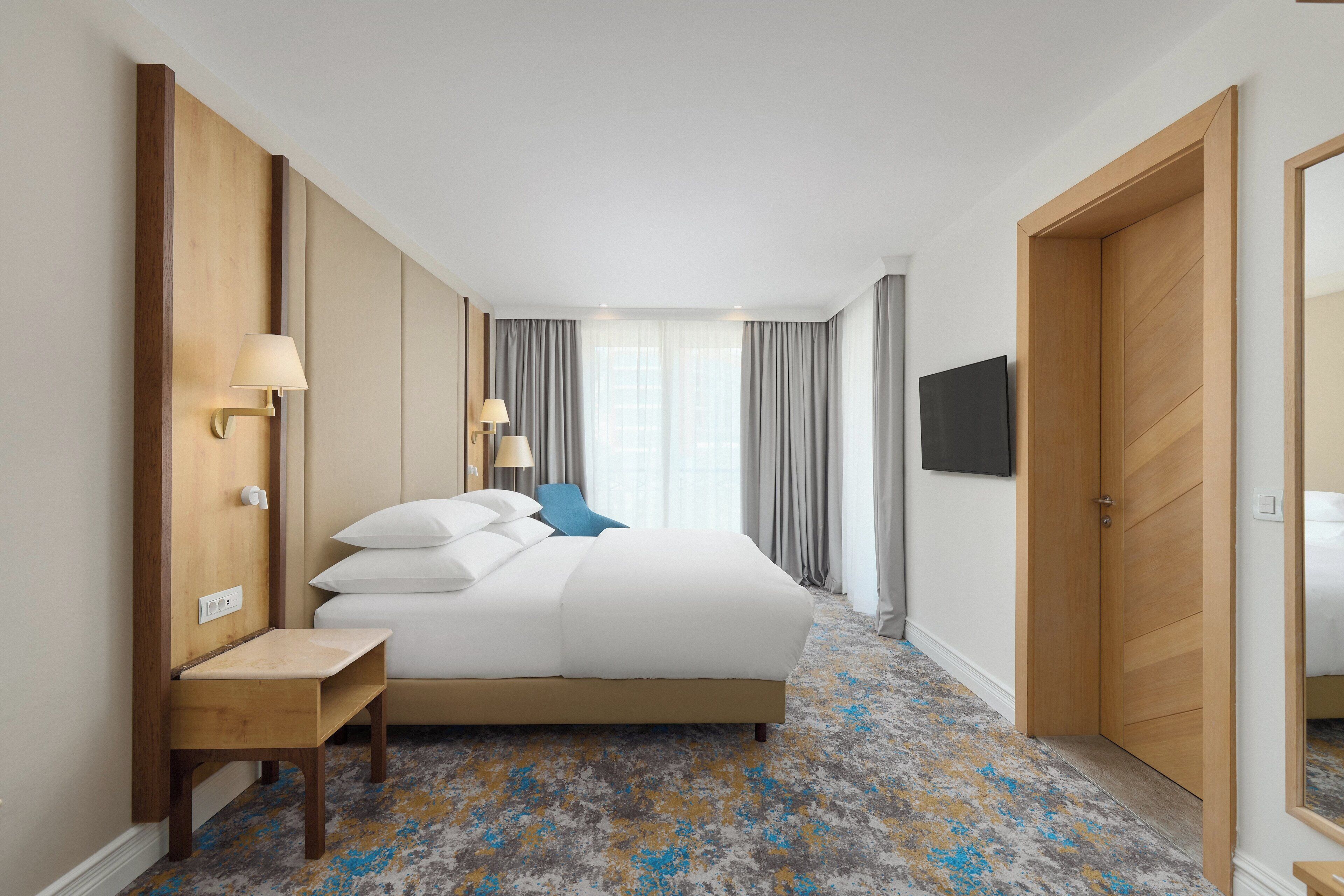 Une chambre d’hôtel avec un lit, des tables de chevet, une télévision et un miroir.