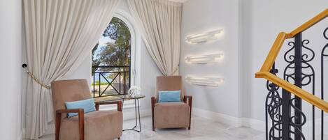 Una habitación con dos sillones, una mesita, un ventanal con cortinas y una escalera con barandilla de metal.