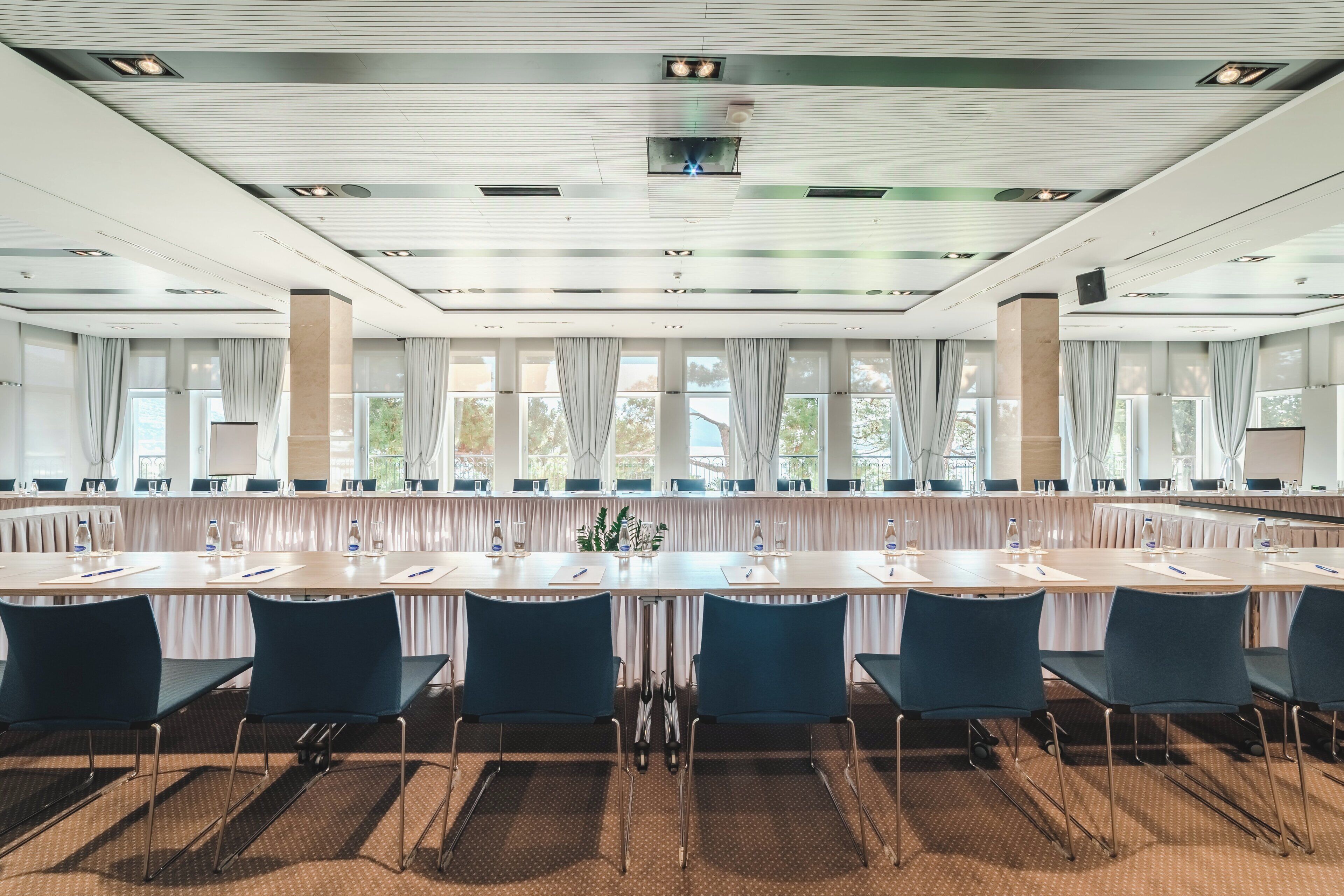 A conference room with a long table, chairs, and a large window with curtains.
