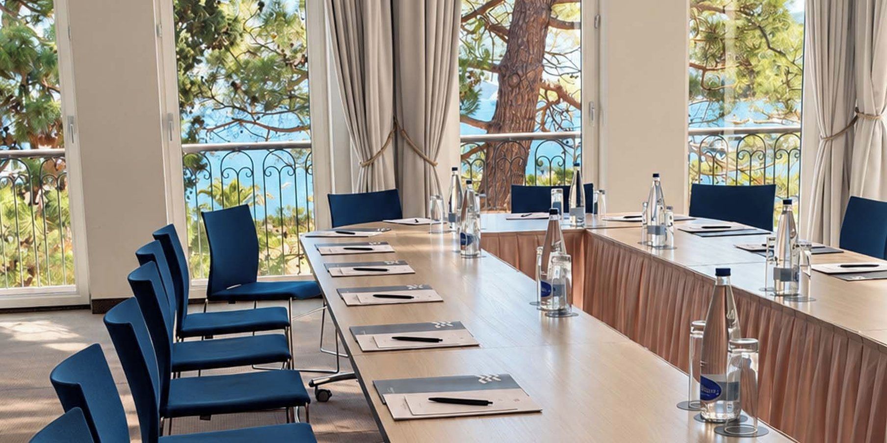 Un salón de conferencias con una larga mesa, sillas y vistas a árboles a través de amplias ventanas.