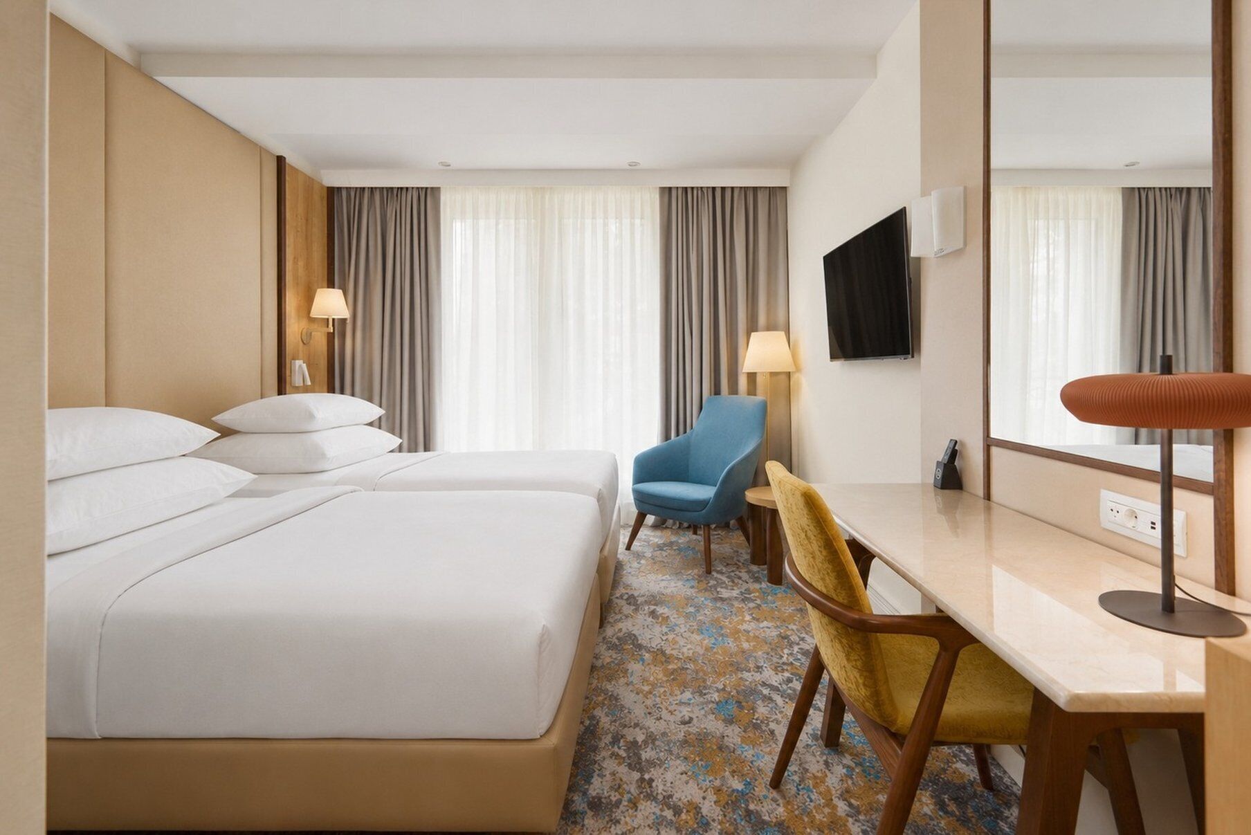 A hotel room with a bed, a desk, a chair, a TV, and a mirror.