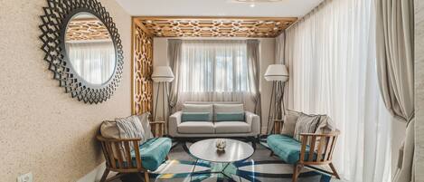 Uma sala de estar com um sofá, duas poltronas, uma mesa de centro, um espelho decorativo e um tapete estampado.