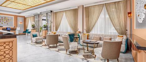 A spacious lobby with a reception desk, seating area, and large windows with curtains.