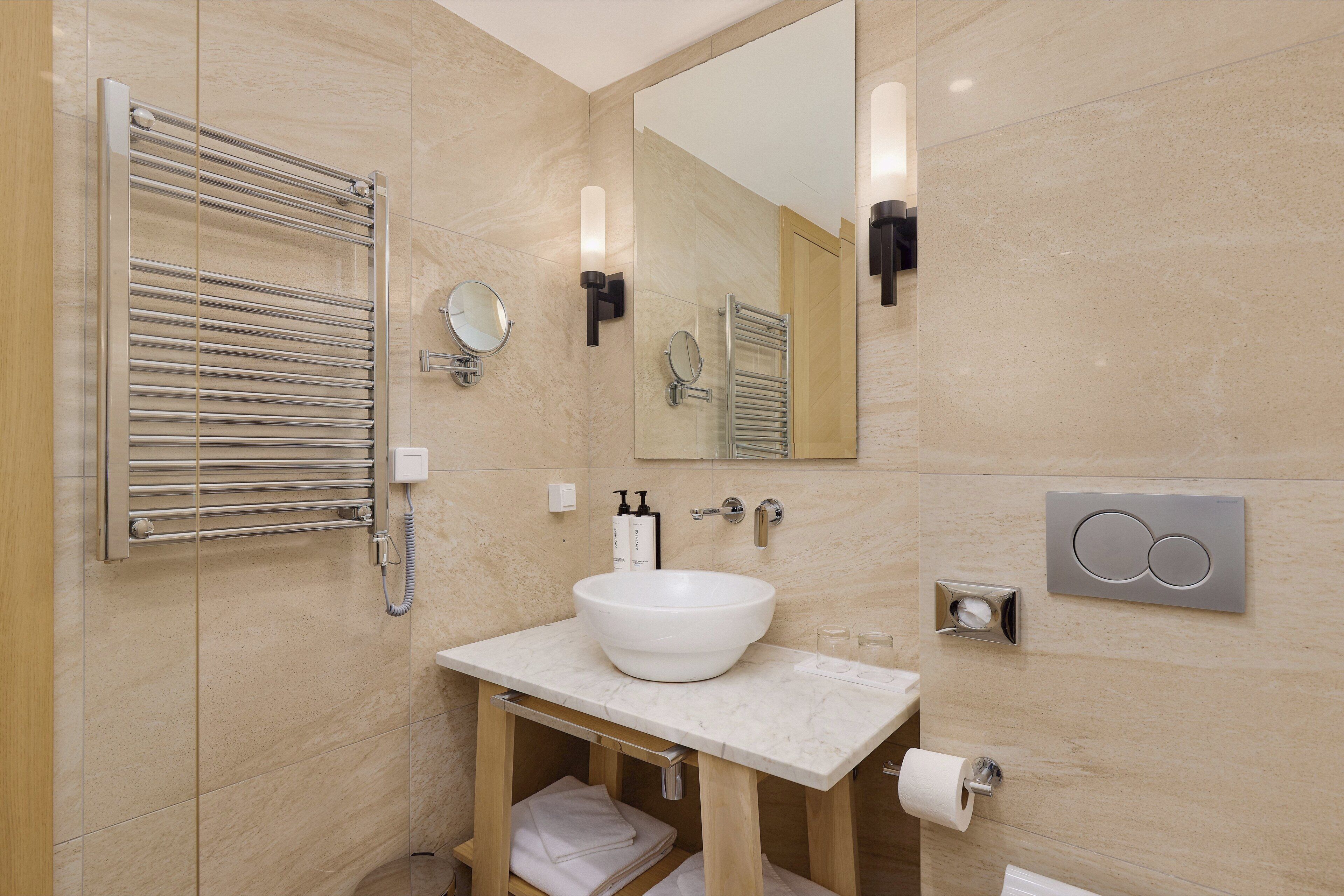 A modern bathroom with a large mirror, a towel rack, a sink with a marble countertop, and a toilet paper holder.