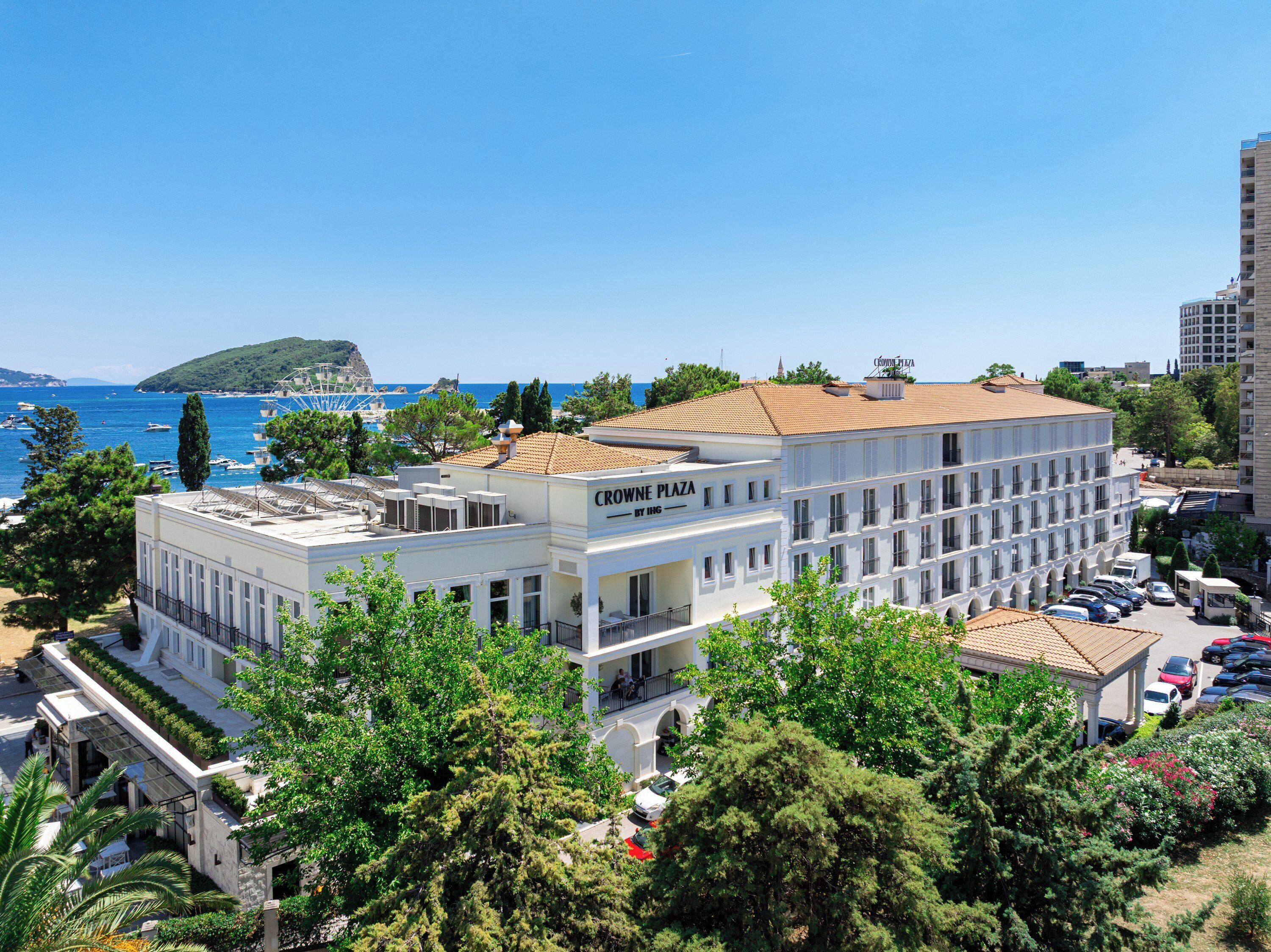 A multi-story building with a sign reading 'CROWN PLAZA' and a view of the sea and a small island in the background.