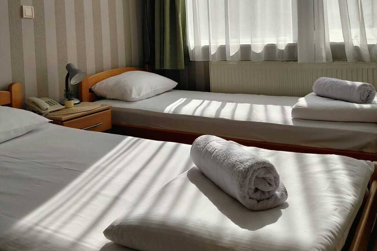 A hotel room with two single beds, a bedside table with a lamp, a telephone, and a radiator.