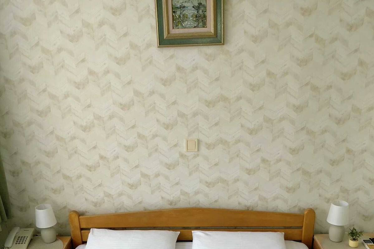A neatly made bed with two pillows, a wooden headboard, and a framed picture on the wall.