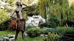 A bronze statue of a woman in a garden with a weeping willow tree and rocks. - Hotel Slodes (Belgrade)