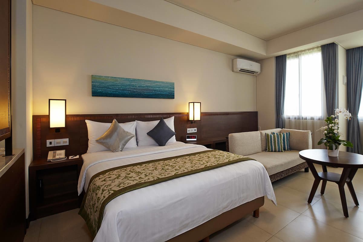 Een hotelkamer met een groot bed, een bank, een eettafeltje en een schilderij aan de muur.