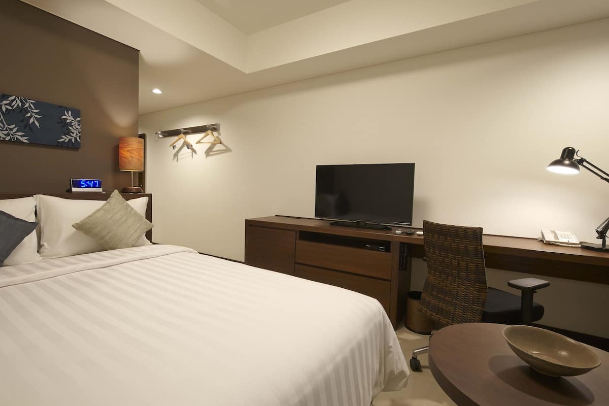 Een hotelkamer met een bed, een bureau, een televisie, een stoel en een kom op het bureau.