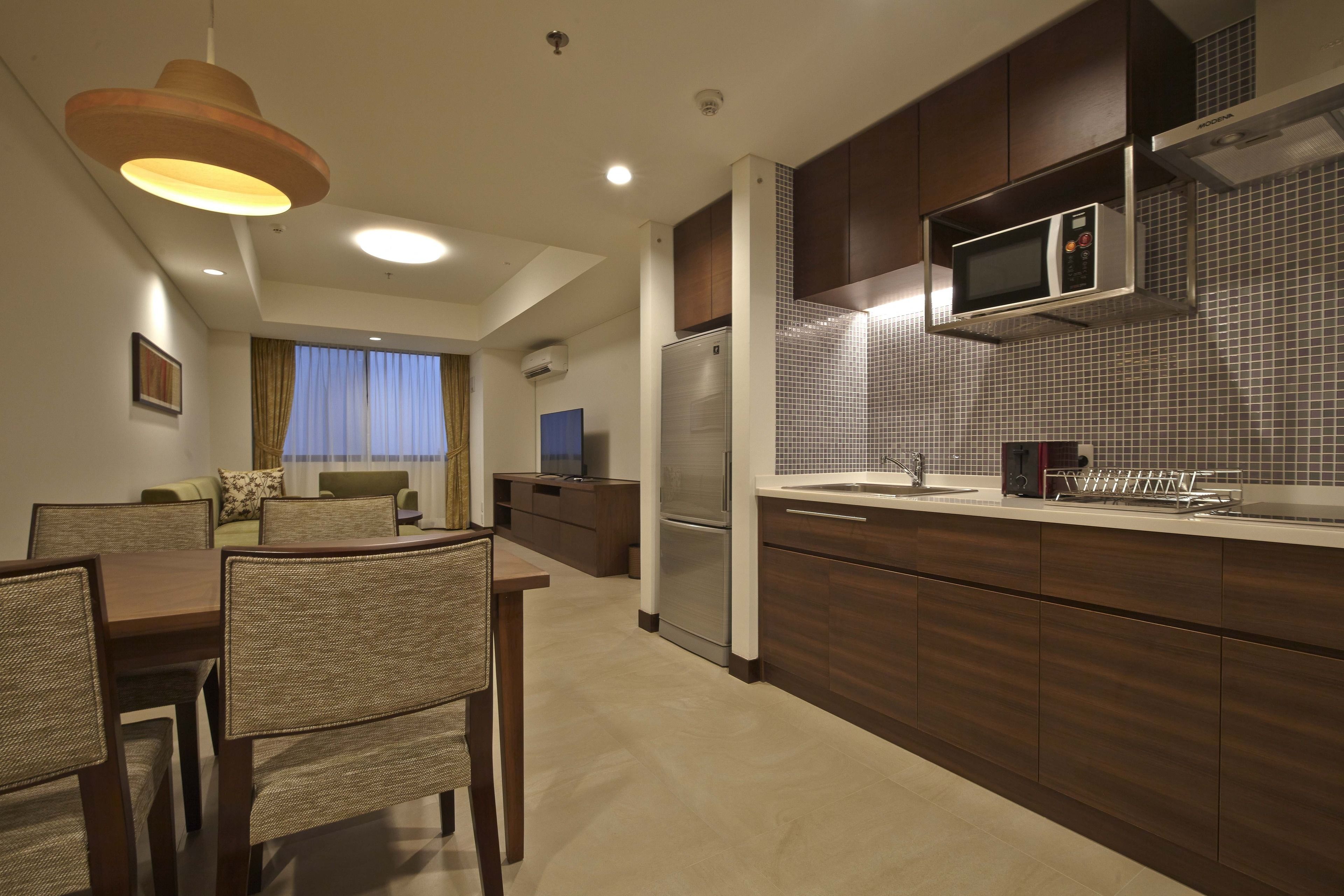 A modern kitchen with dark wood cabinets, a stainless steel refrigerator, and a microwave. There is a dining area with a table and chairs.