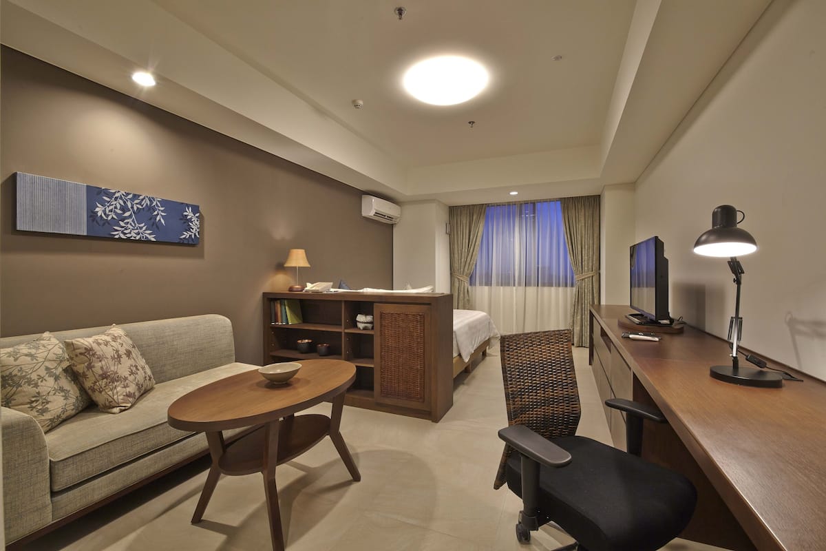 Een hotelkamer met een bank, een tafeltje, een bureau met stoel, een televisie en een raam met gordijnen.