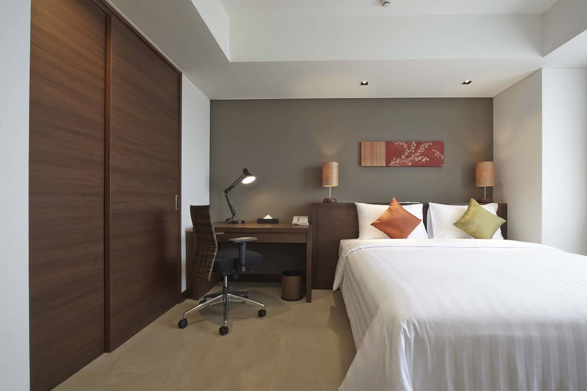 Een hotelkamer met een bed, bureau, stoel, lamp en een kunstwerk aan de muur.