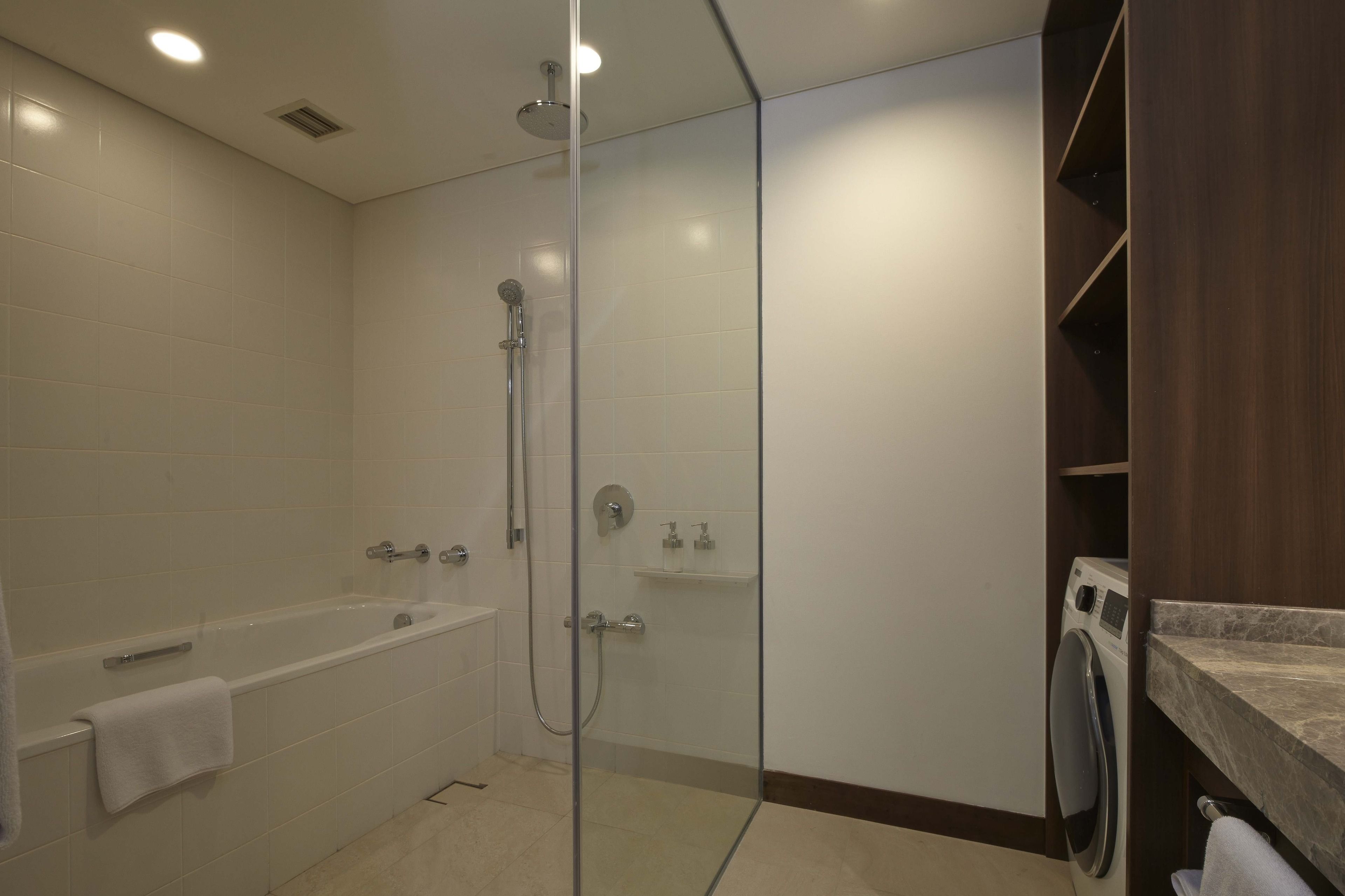 A modern bathroom with a glass-enclosed shower, a bathtub, and a built-in washing machine.