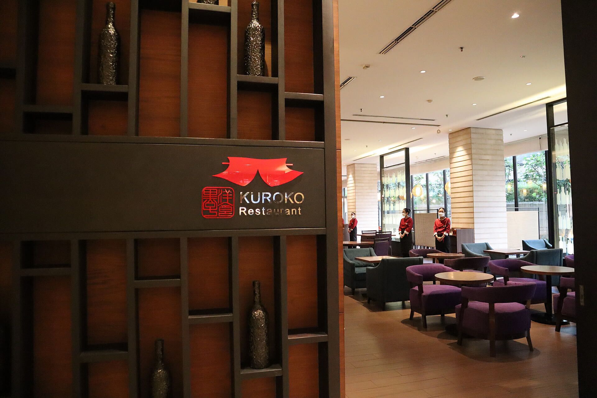 A restaurant interior with a sign for Kuroko Restaurant, featuring a modern design with wooden panels and purple seating.