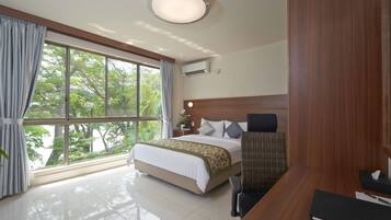Quarto de hotel com uma cama grande, uma mesa, uma cadeira e vista para árvores pela janela.