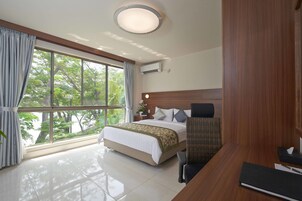 Quarto de hotel com uma cama grande, uma mesa, uma cadeira e vista para árvores pela janela.