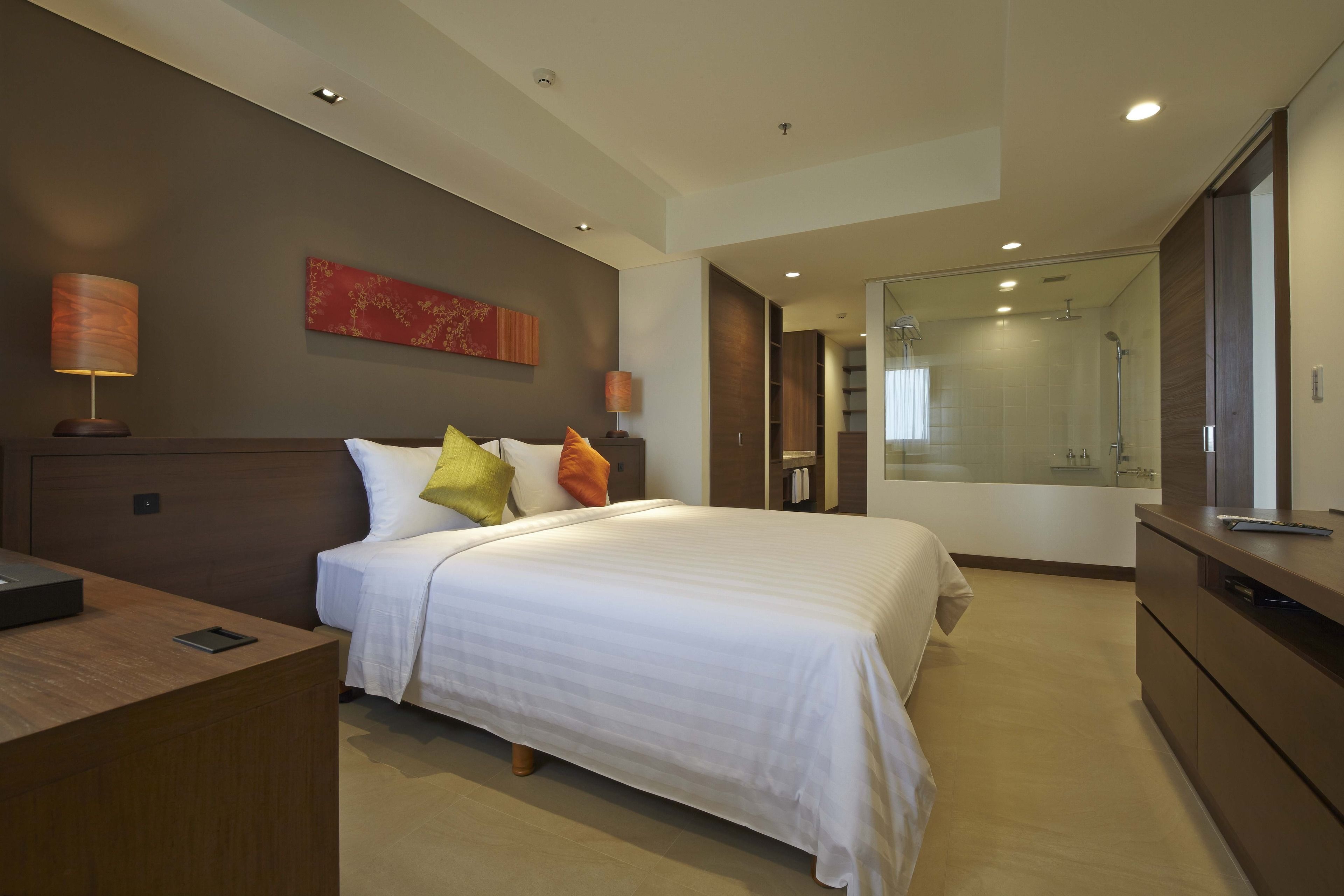 A modern hotel room with a large bed, bedside lamps, a desk, and a walk-in closet.