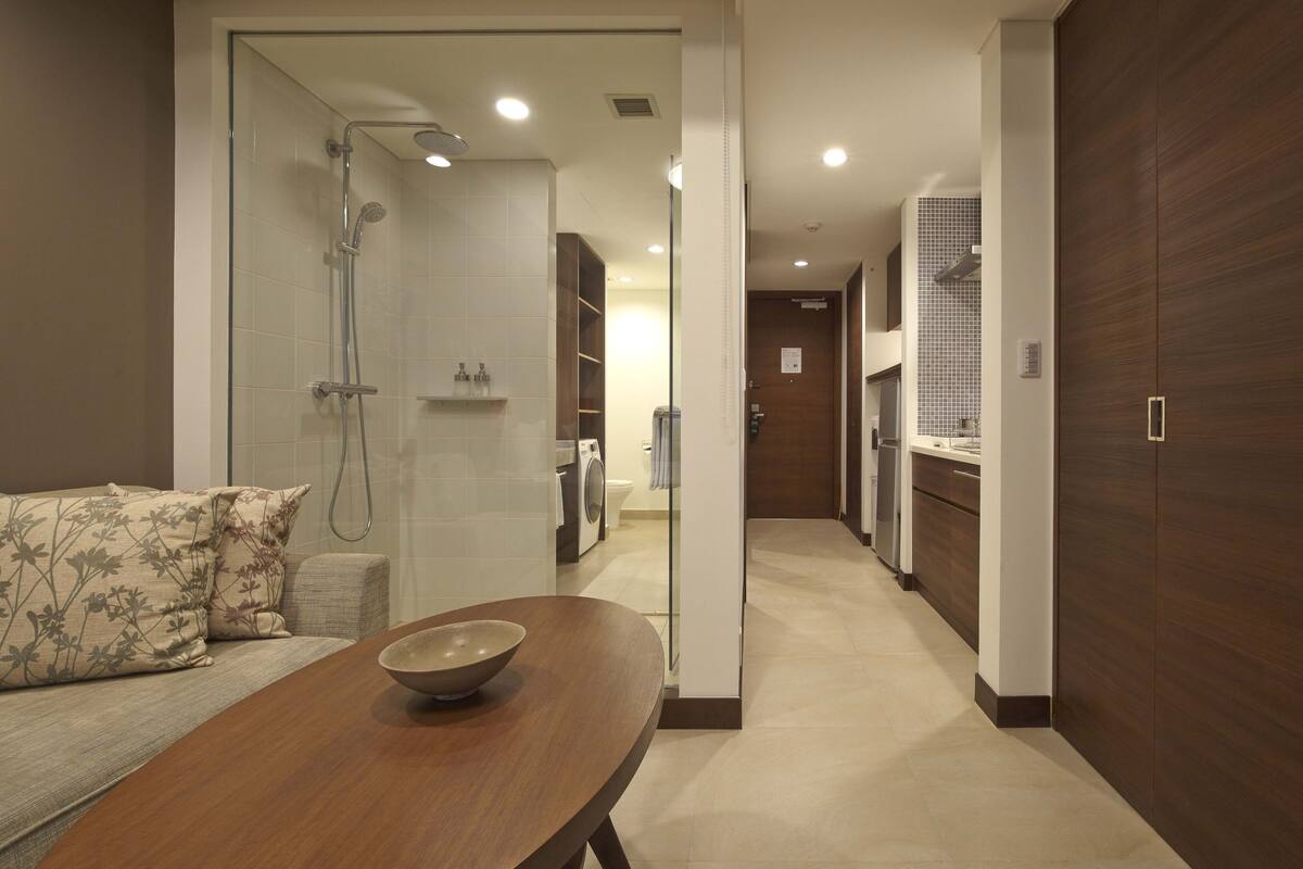 Een moderne badkamer met een douche, toilet en wastafel. Op de voorgrond staat een houten tafeltje met een kom.
