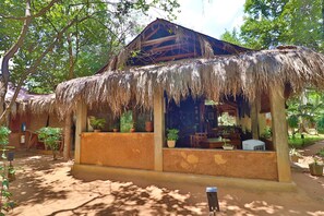 A rustic hut with a thatched roof, surrounded by trees and potted plants. - The Other Corner (Habarana)