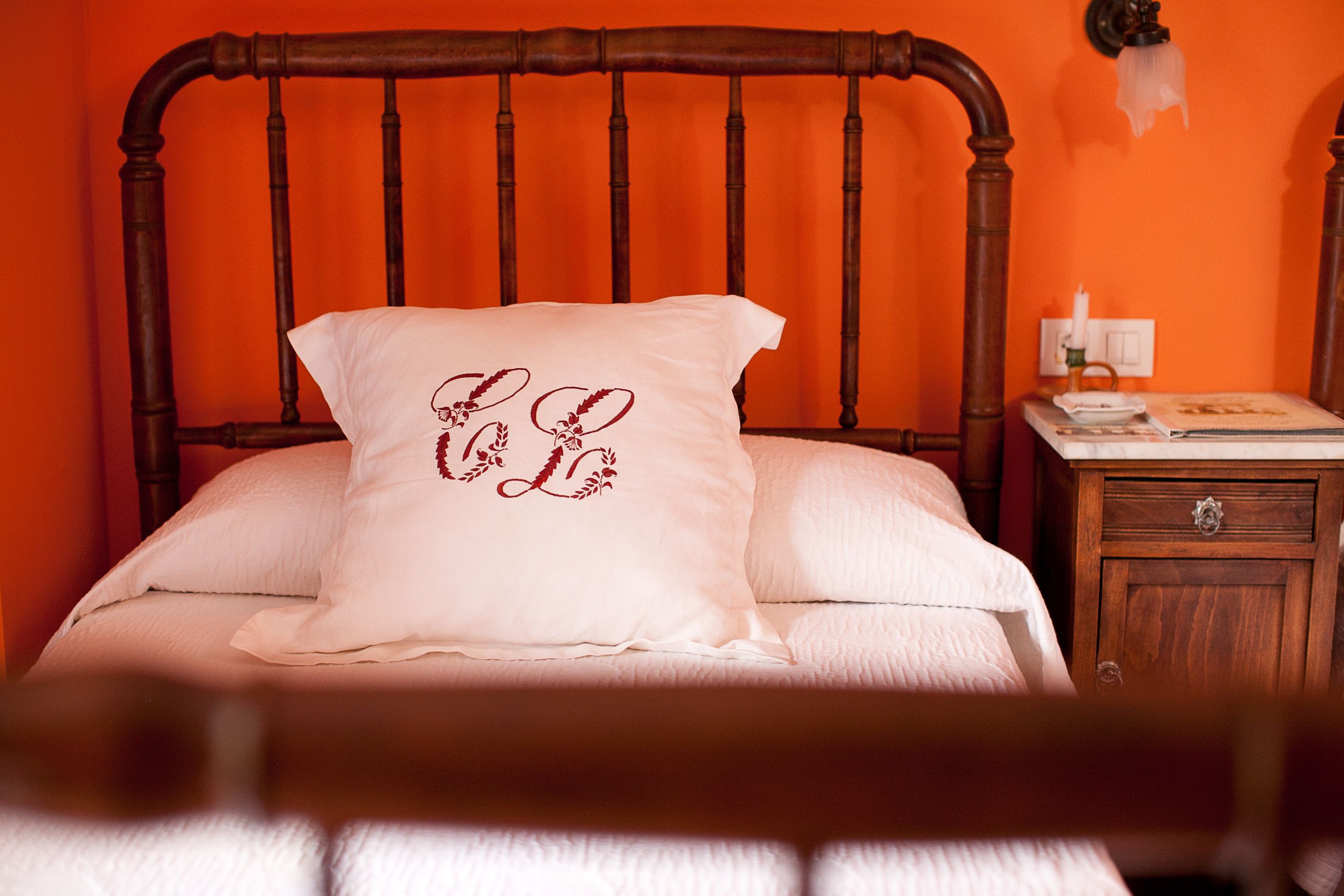 A bed with a wooden headboard, a white pillow with a floral design, and a bedside table with a lamp and a book.