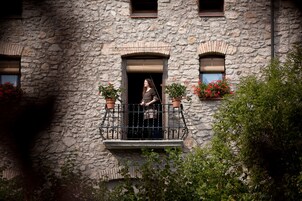 Un edificio de piedra con un balcón adornado con plantas en macetas y una ventana con contraventanas.