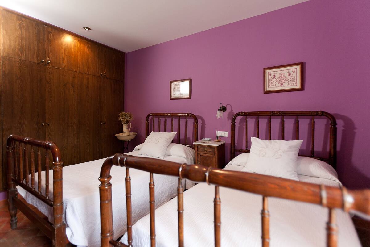 Una habitación con dos camas de madera, un armario de madera, una mesita de noche pequeña con una lámpara y un cuadro enmarcado en la pared.