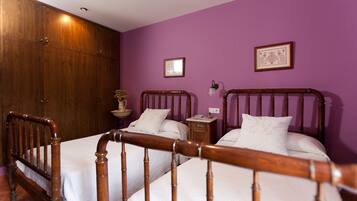 A room with two wooden beds, a wooden wardrobe, a small bedside table with a lamp, and a framed picture on the wall.