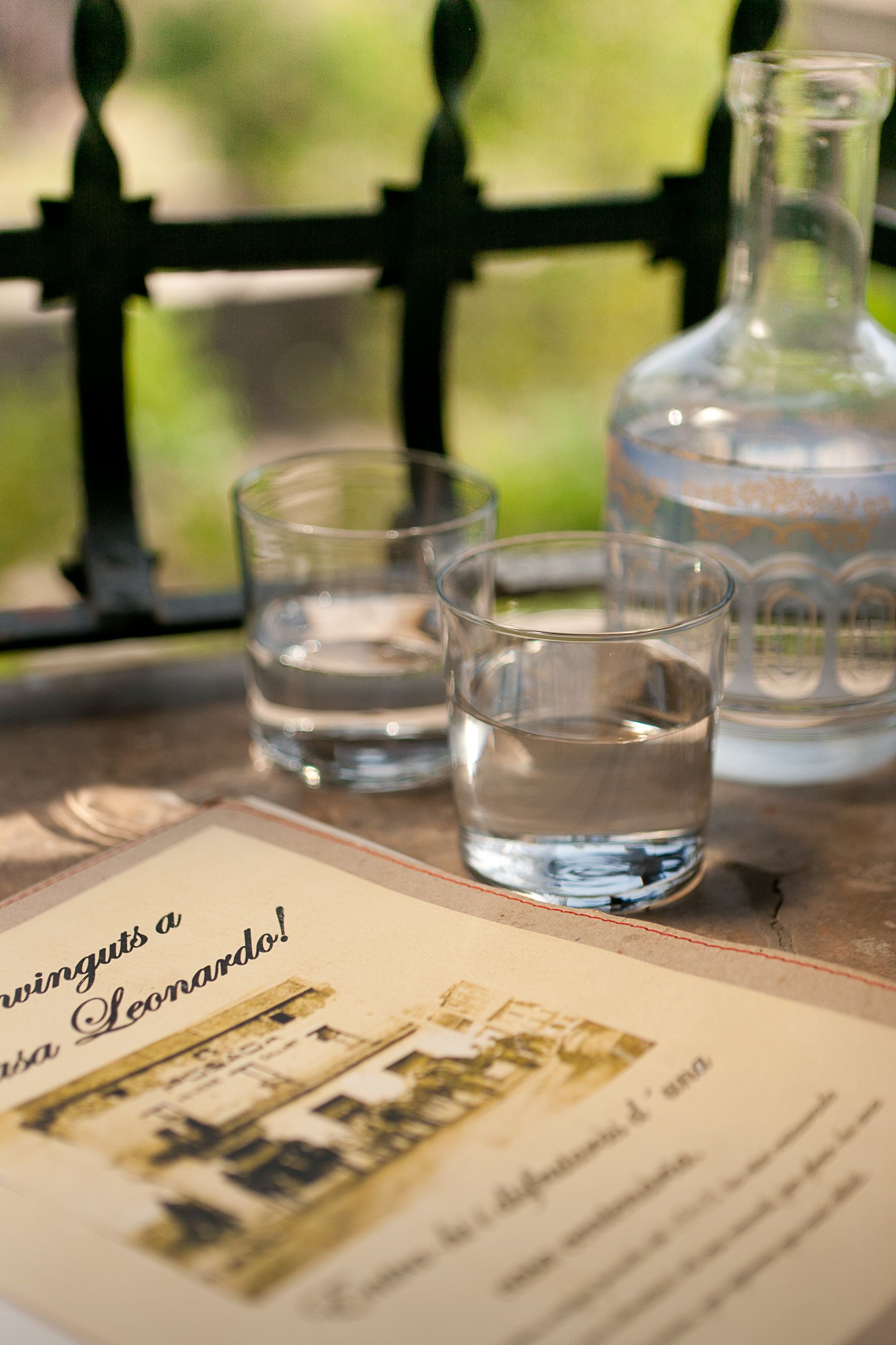 A table with a glass bottle and two glasses of water, a menu, and a view through a window.