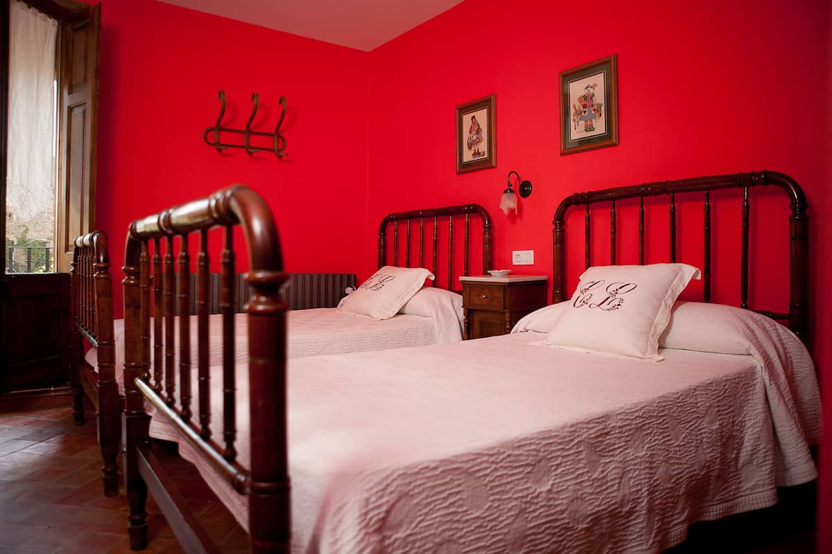 Una habitación con dos camas de madera, paredes rojas y una mesita de noche pequeña.