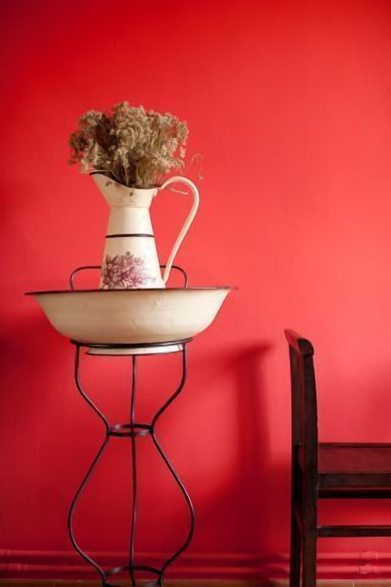 Un vase blanc contenant des fleurs séchées, posé sur une table blanche devant un mur rouge.