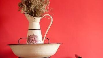 Un vase blanc contenant des fleurs séchées, posé sur une table blanche devant un mur rouge.