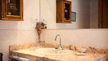 A bathroom with a marble sink, a mirror, a wooden cabinet, and a vase with dried flowers.