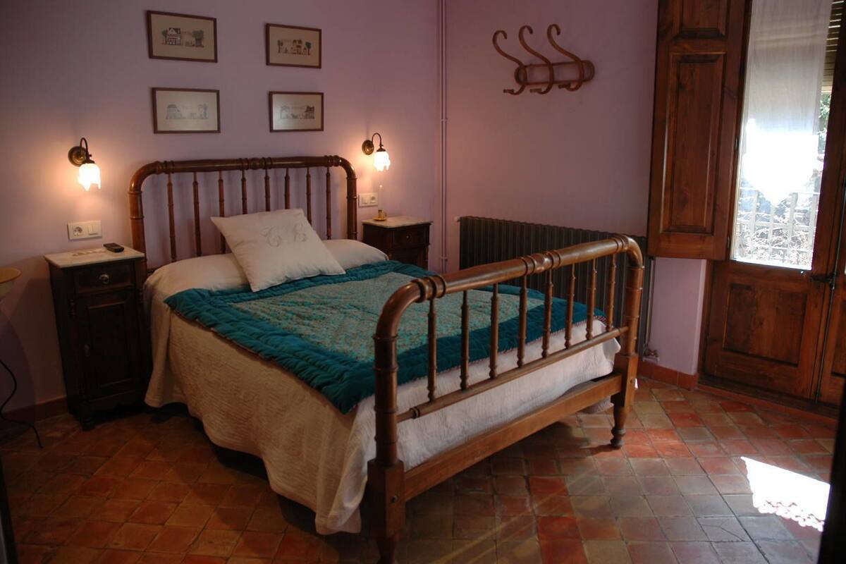 Un dormitorio con cama de madera, dos mesitas de noche, un radiador y una ventana con vistas.