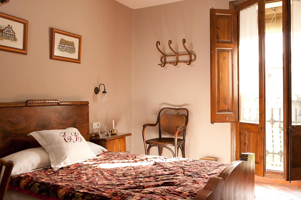 Un dormitorio con una cama de madera, una silla, una mesita de noche y un ventanal con vistas.