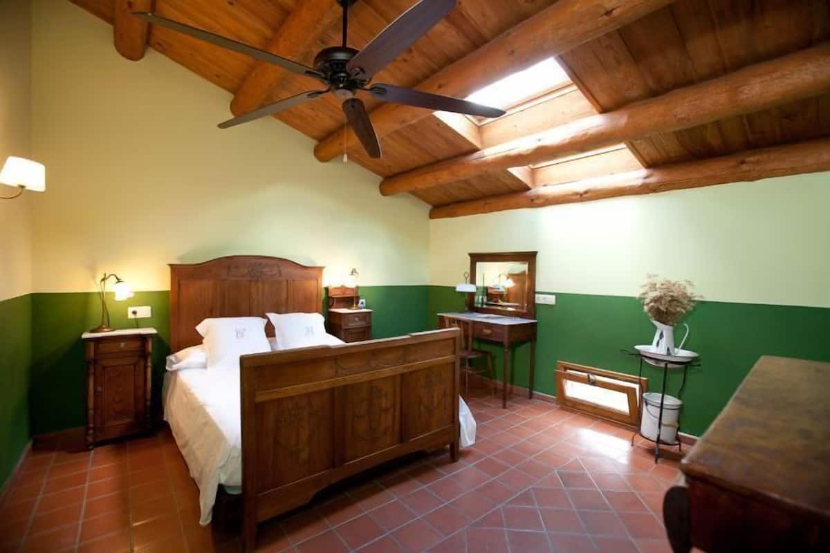 Un dormitorio con un ventilador de techo de madera, una cama, un escritorio y una silla.