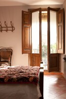 Un dormitorio con una cama, una silla y una puerta abierta que da a un balcón.