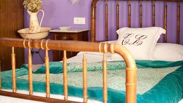 A bedroom with a wooden bed frame, a teal and white bedspread, a white pillow with embroidered text, and a vase with flowers on a nightstand.
