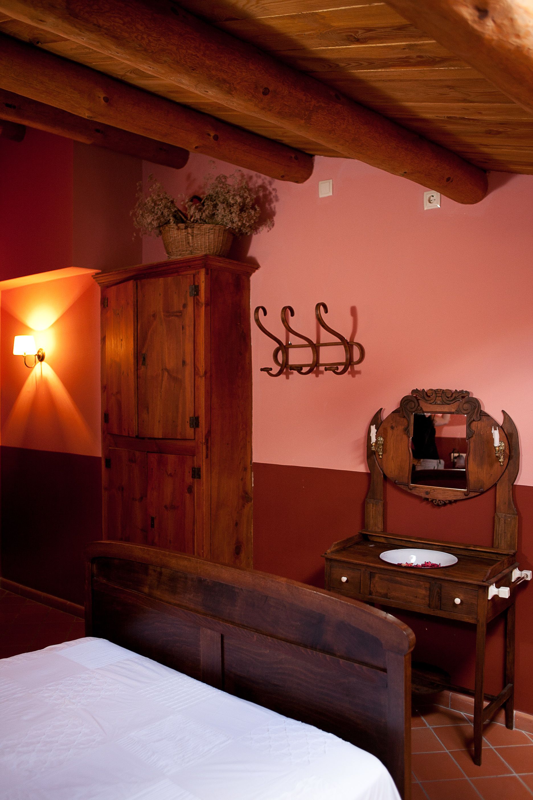 Un dormitorio con una cama de madera, una mesita de noche con espejo, un estante en la pared con flores y una lámpara de pared.