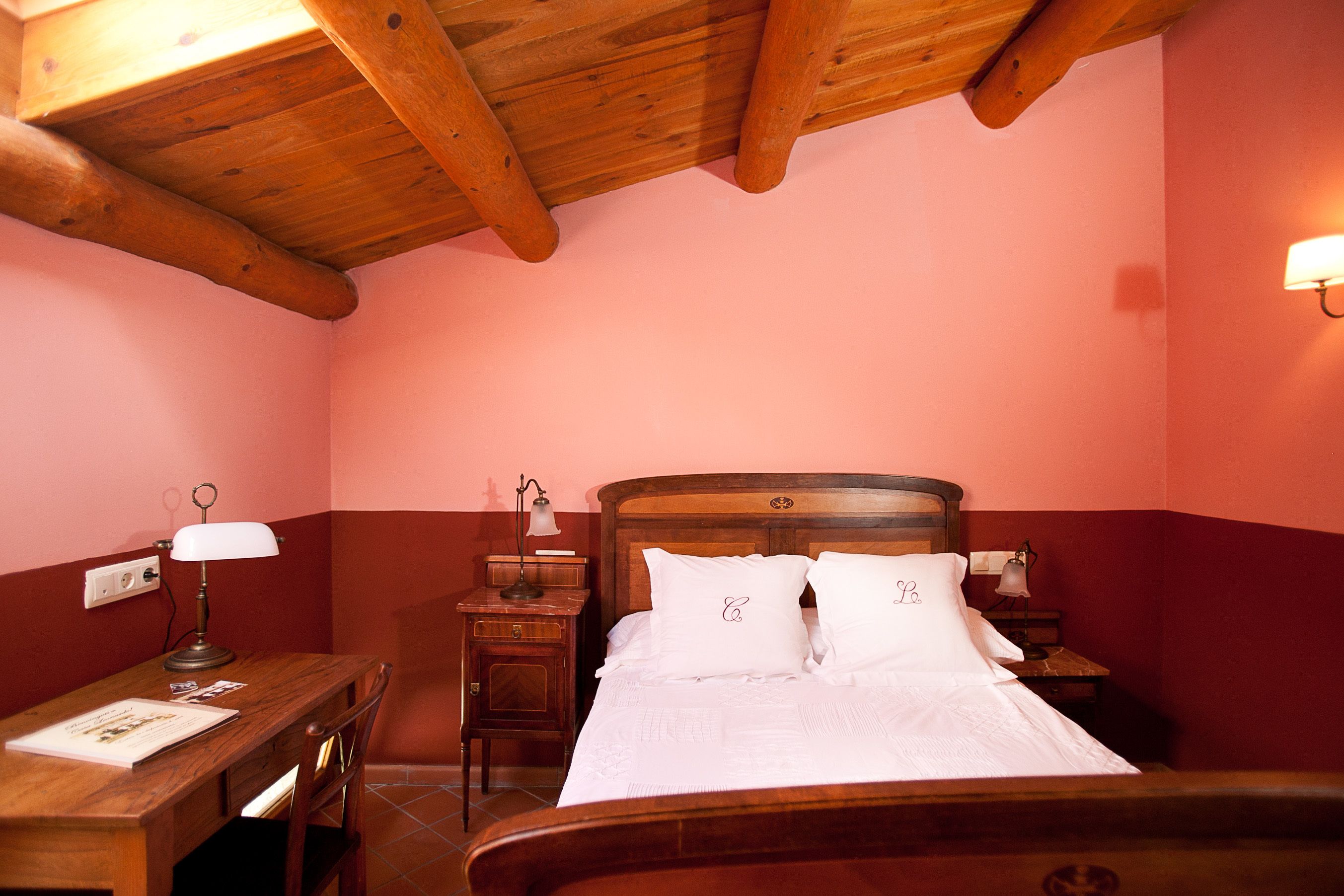 Un dormitorio con cama de madera, un escritorio, una silla, una mesita de noche y una lámpara.