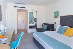 A hotel room with a bed, a desk with a chair, a mirror, a painting, and a bowl of fruit. - Americana Hotel (Eilat)
