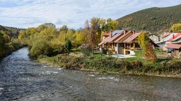 Un hotel a orillas del río con edificios de piedra, piscina y vistas al río y a las colinas.